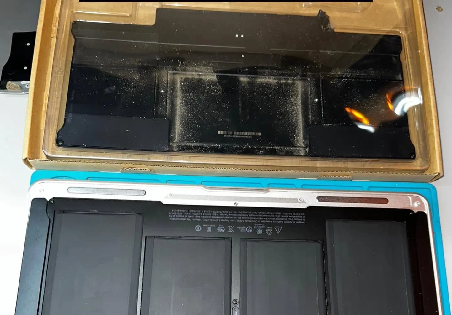Batería nueva instalada en una MacBook Air, con la batería antigua retirada en su caja